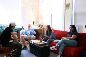 Four students eating pizza and chatting in a dorm room